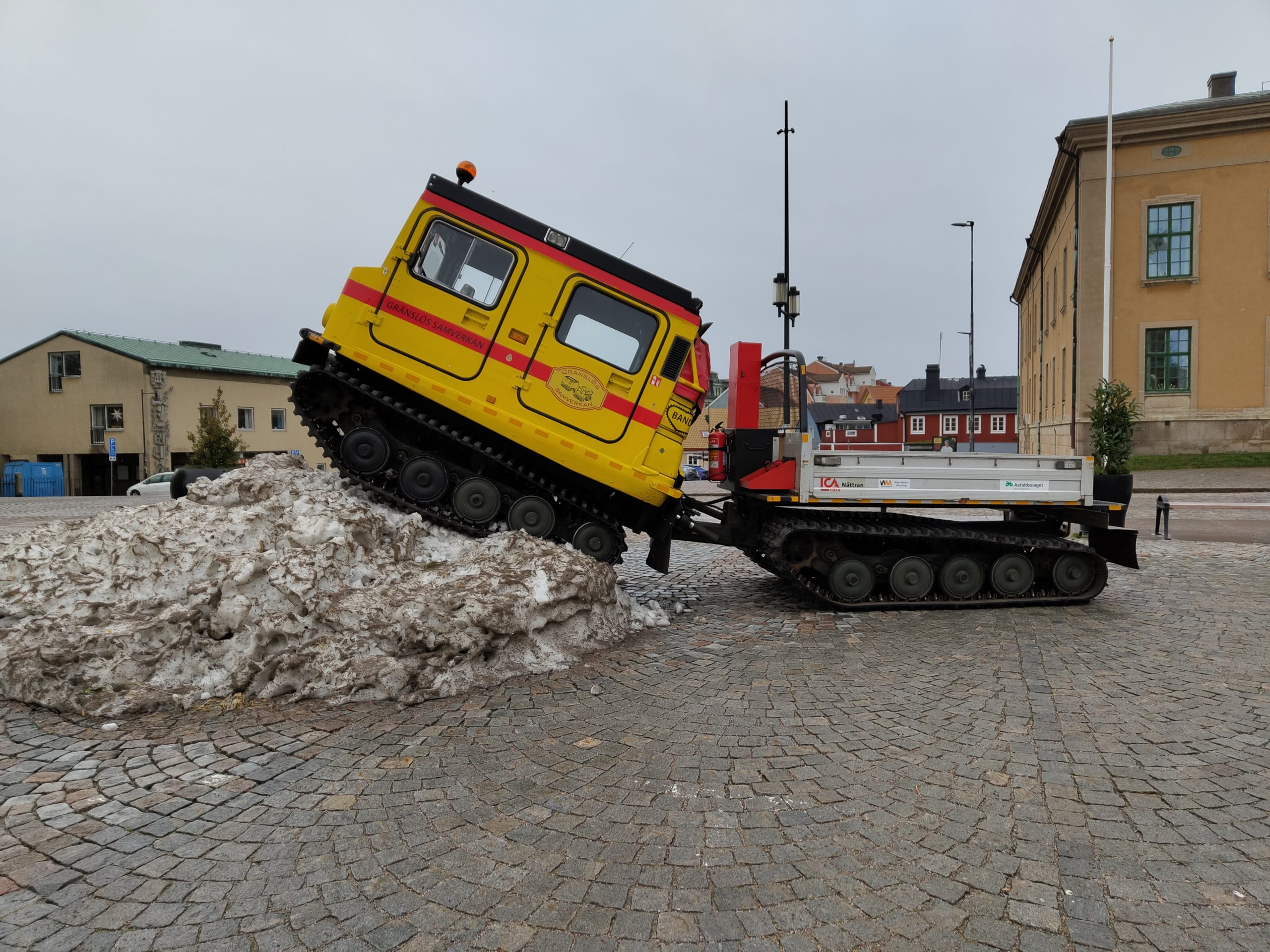 Bandvagn med flak halvvägs upp i snöhög.